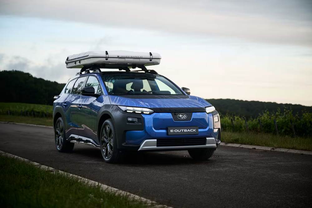 Blue Subaru E-Outback with a roof tent on a road between vineyards
