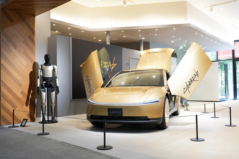 Tesla Cybercab auriu, cu ușile deschise, expus într-un showroom Tesla din Japonia, lângă robotul Optimus