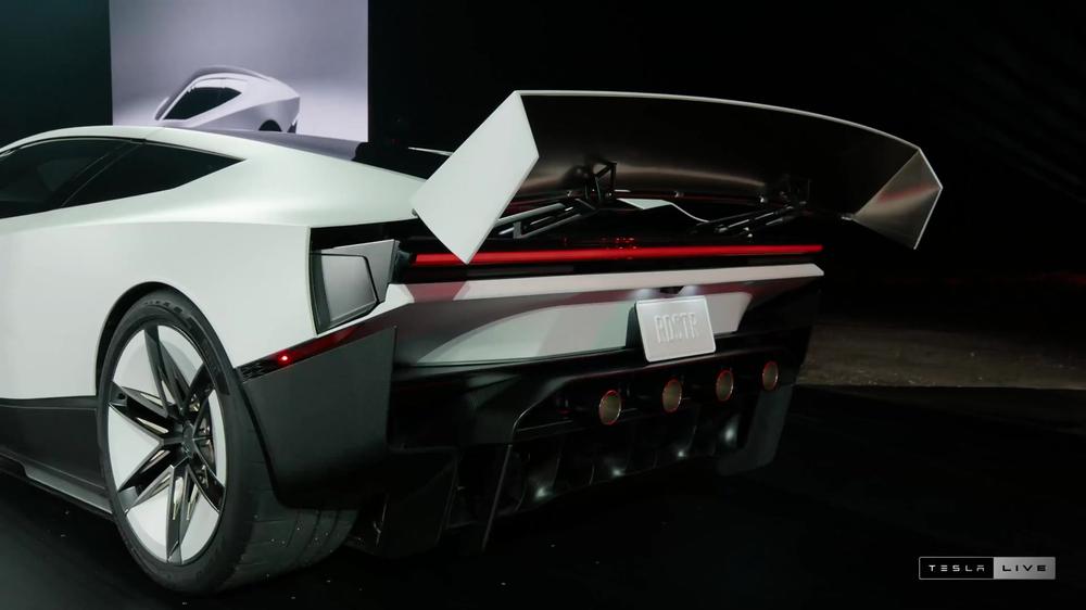 Rear of the white Tesla Roadster with its wing raised and diffuser visible on the event stage