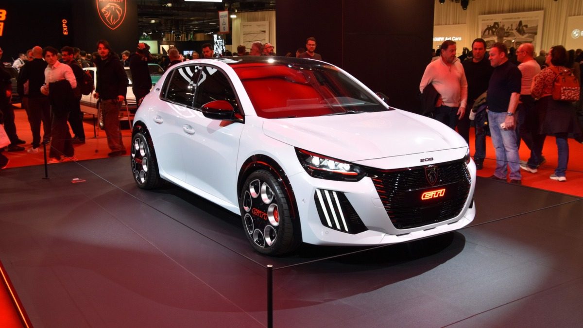 Peugeot E-208 GTi alb, cu dungi și accente roșii, expus pe un stand la un salon auto