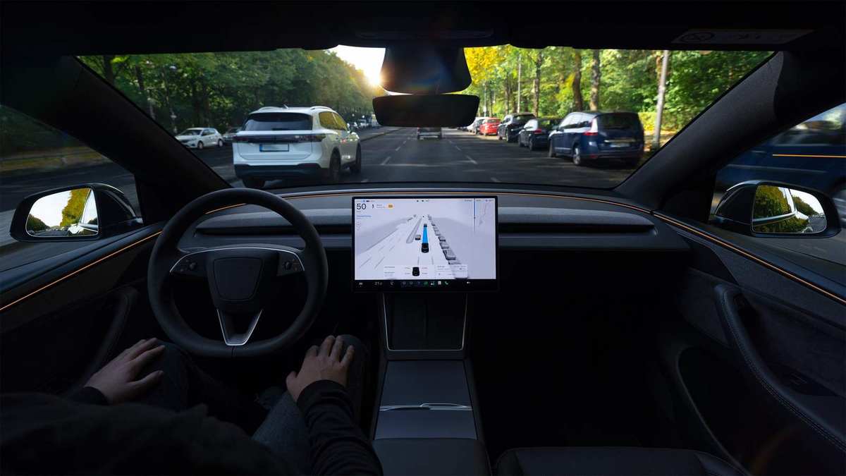 Vedere din habitaclul unei Tesla, cu mâinile șoferului lângă volan și vizualizarea sistemului pe ecranul central