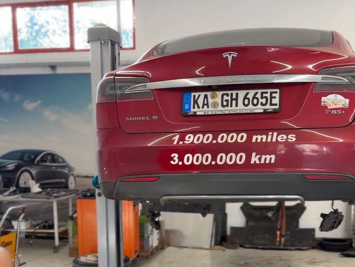 Red Tesla Model S P85+ on a lift, with 1,900,000 miles and 3,000,000 km written on the rear bumper