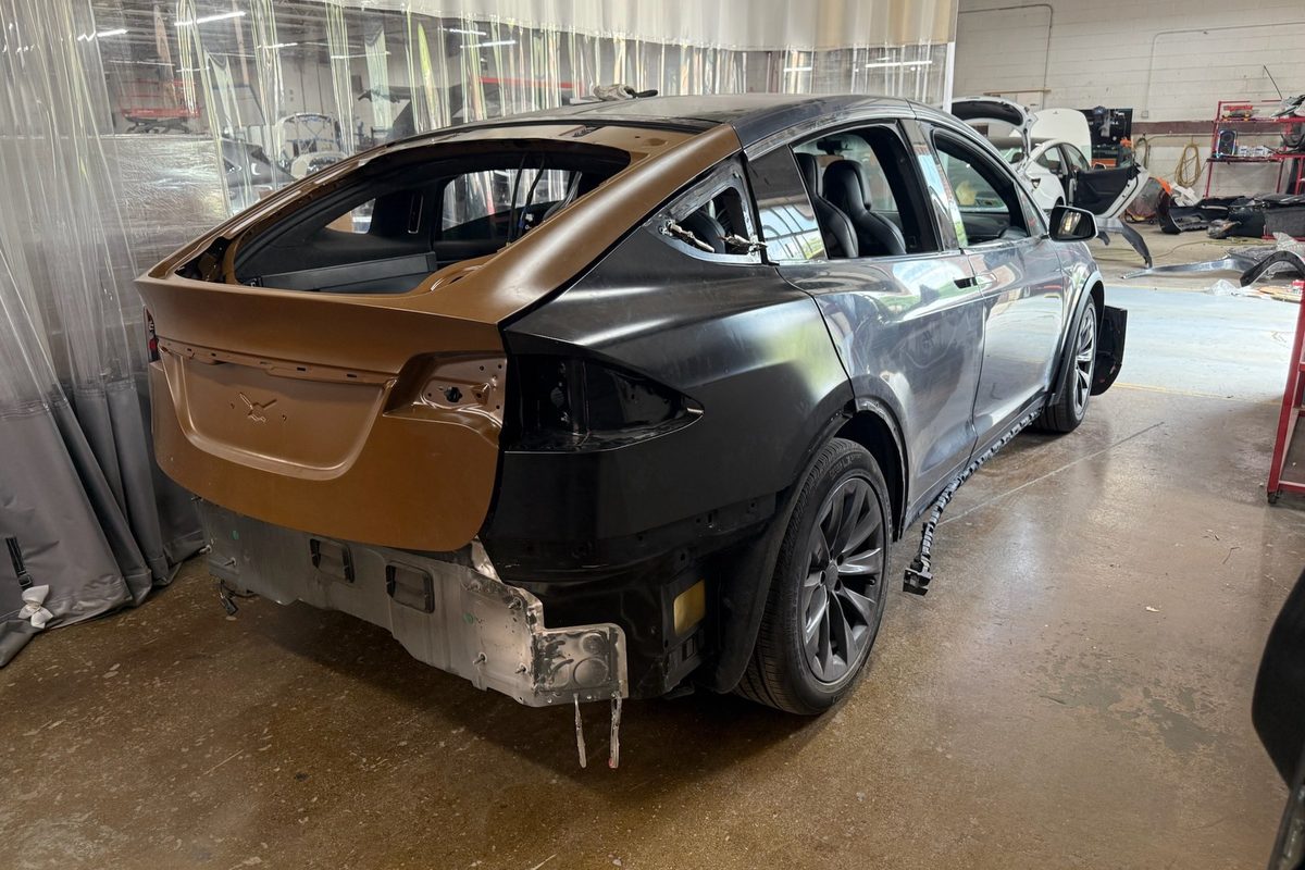 A Tesla Model X with its rear end stripped, under repair in a body shop